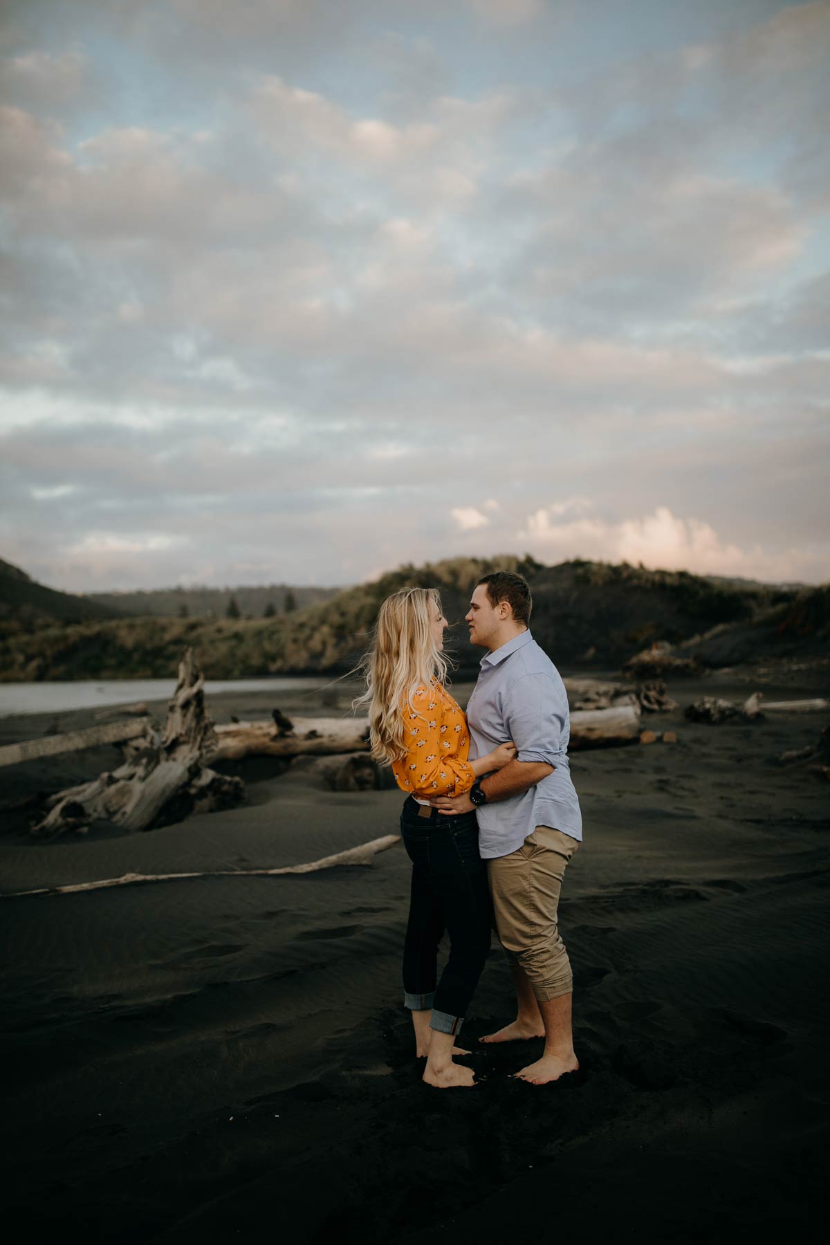 couple embracing at muriwai beach auckland new zealand during a golden light evening lifestyle engagment pre-wedding photoshoot session by sarah weber photography